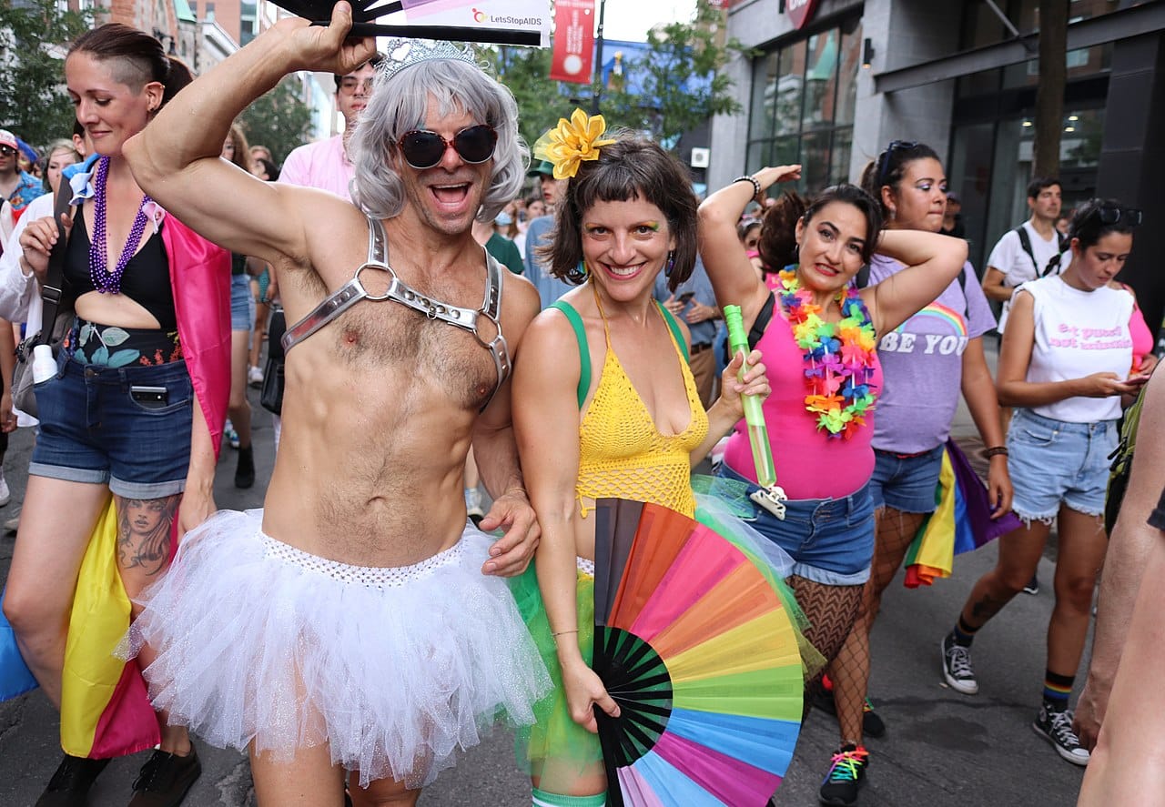 Participants souriants et costumés à la marche de la Fierté de Montréal 2022, vêtus de tenues vives et originales, portant des accessoires arc-en-ciel et célébrant la diversité et l’inclusion dans la rue.